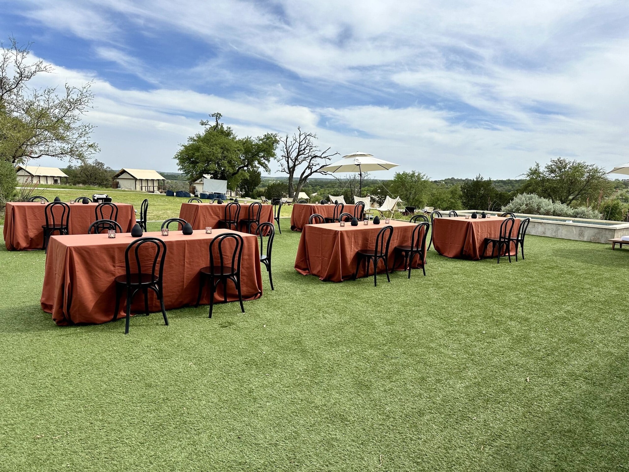 Outdoor group dining at Camp Hideaway Fredericksburg — tables set on the lawn with glamping tents and Hill Country views